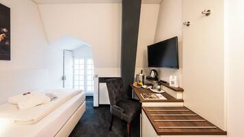 A hotel room with a bed, a desk with a flat-screen TV, a chair, and a small kitchenette.