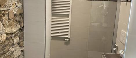 A bathroom with a stone wall, a white toilet, a shower, and a towel rack.