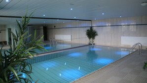 Una piscina interior con suelo de baldosas, una escalera de metal y una planta en maceta.