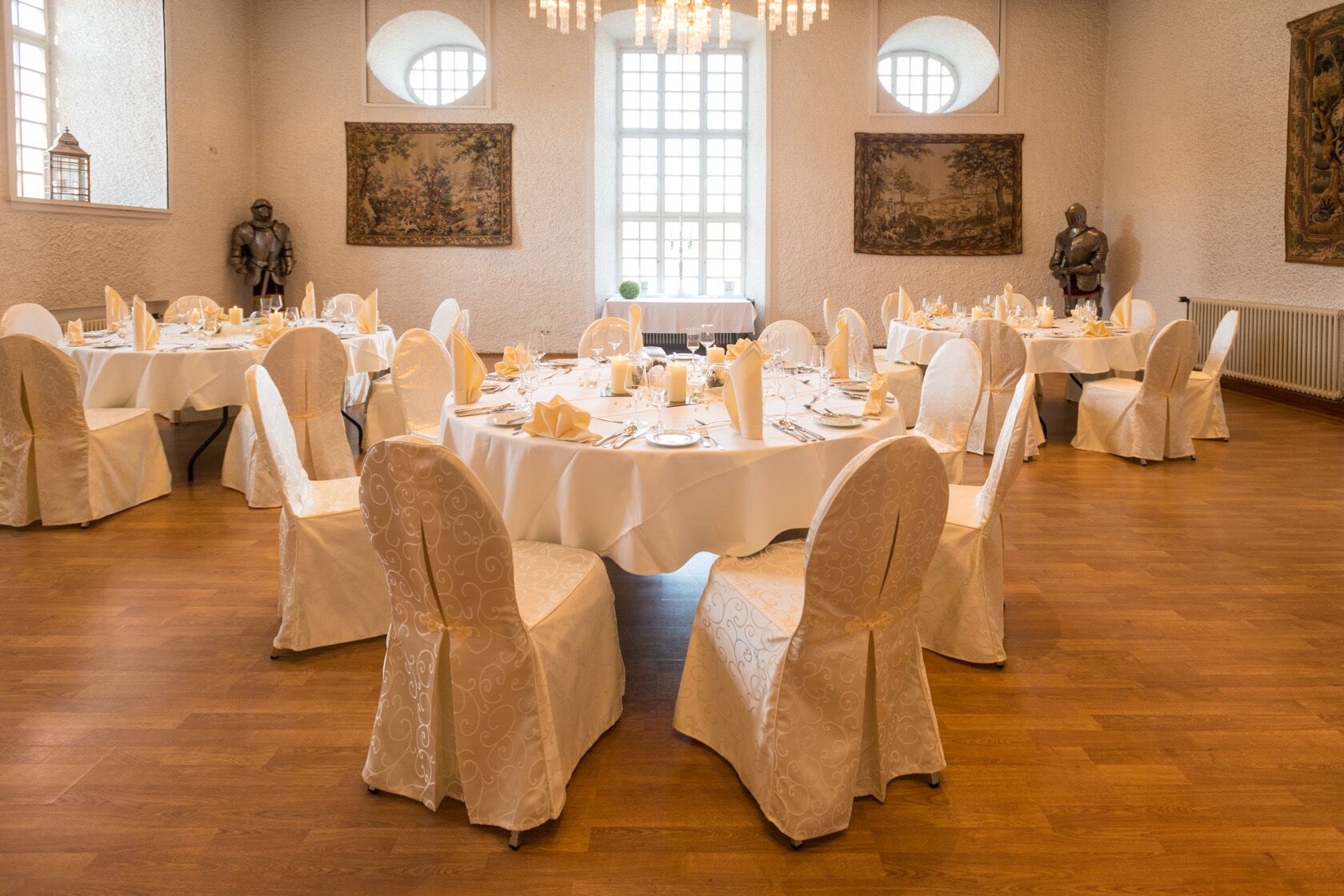 Ein Festsaal mit runden Tischen, weißen Tischdecken und mit weißen Hussen bezogenen Stühlen.