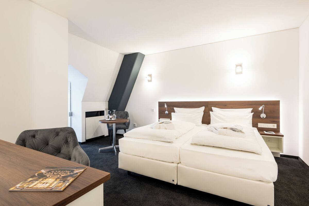 A hotel room with a bed, a desk, a chair, and a small table.