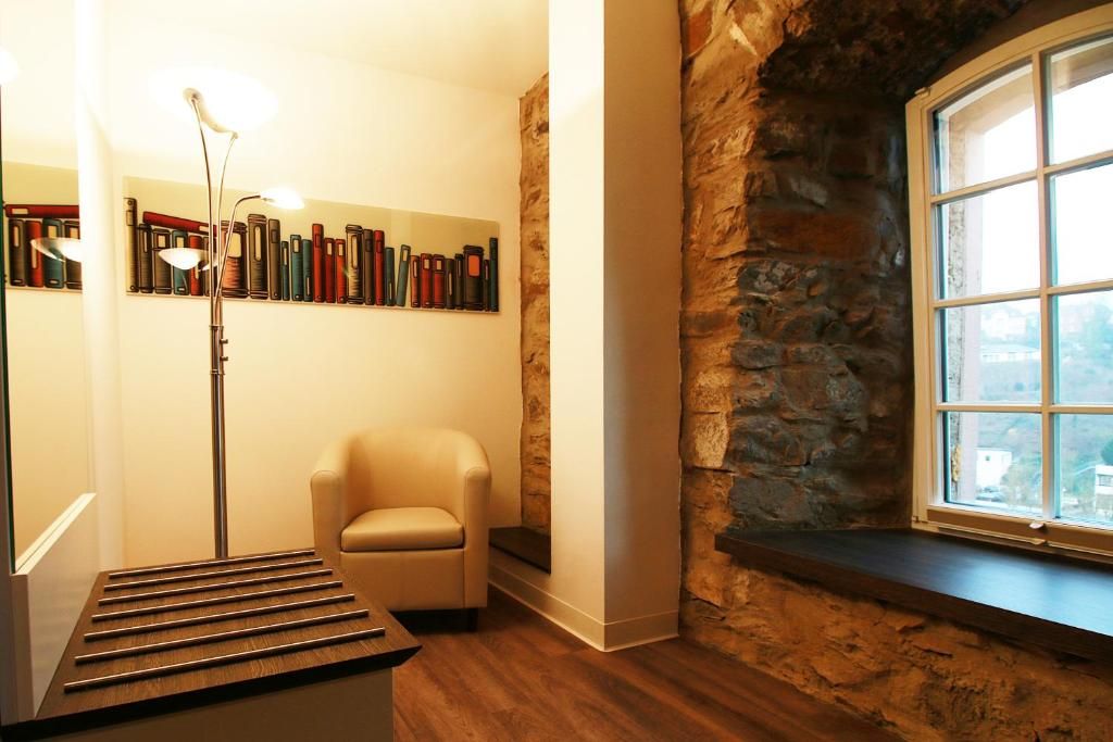 Une pièce avec un mur en pierre, une fenêtre, une bibliothèque, une chaise et un lampadaire.