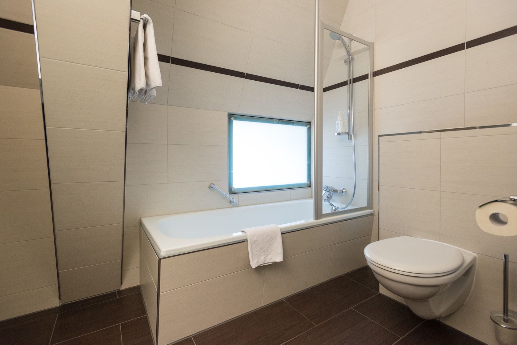 A modern bathroom with a shower, toilet, and a window above the sink.