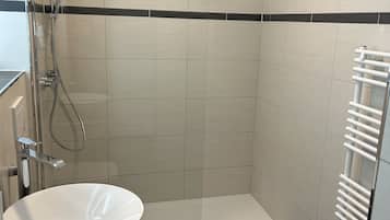 Un baño con un lavamanos blanco, una ducha con cerramiento de vidrio y un toallero blanco.