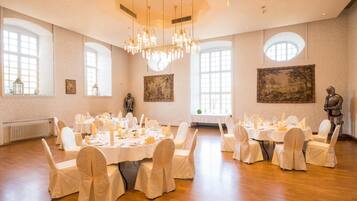A banquet hall with round tables, white chairs, chandeliers, and artwork on the walls.