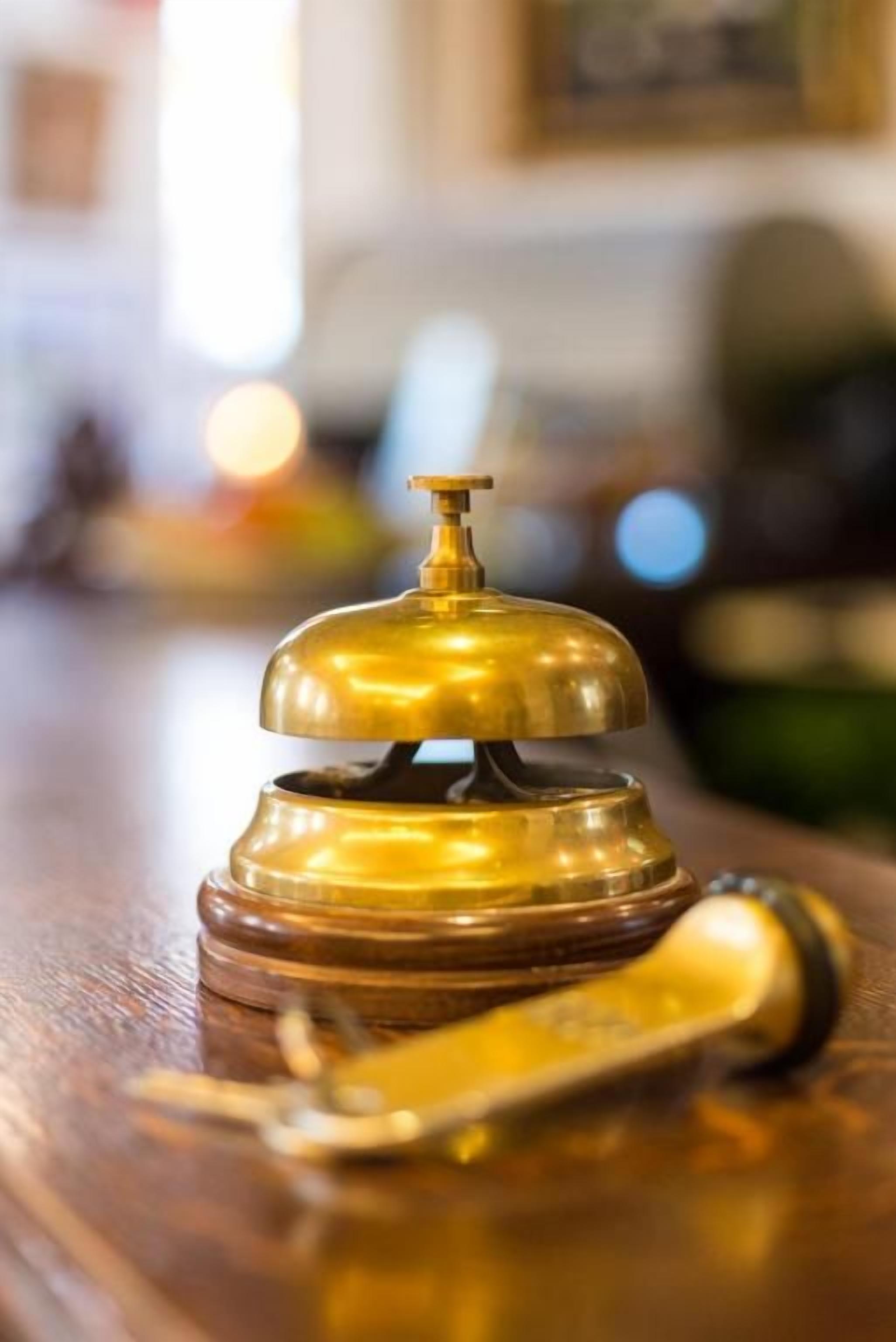 A brass bell and a telephone on a wooden surface.