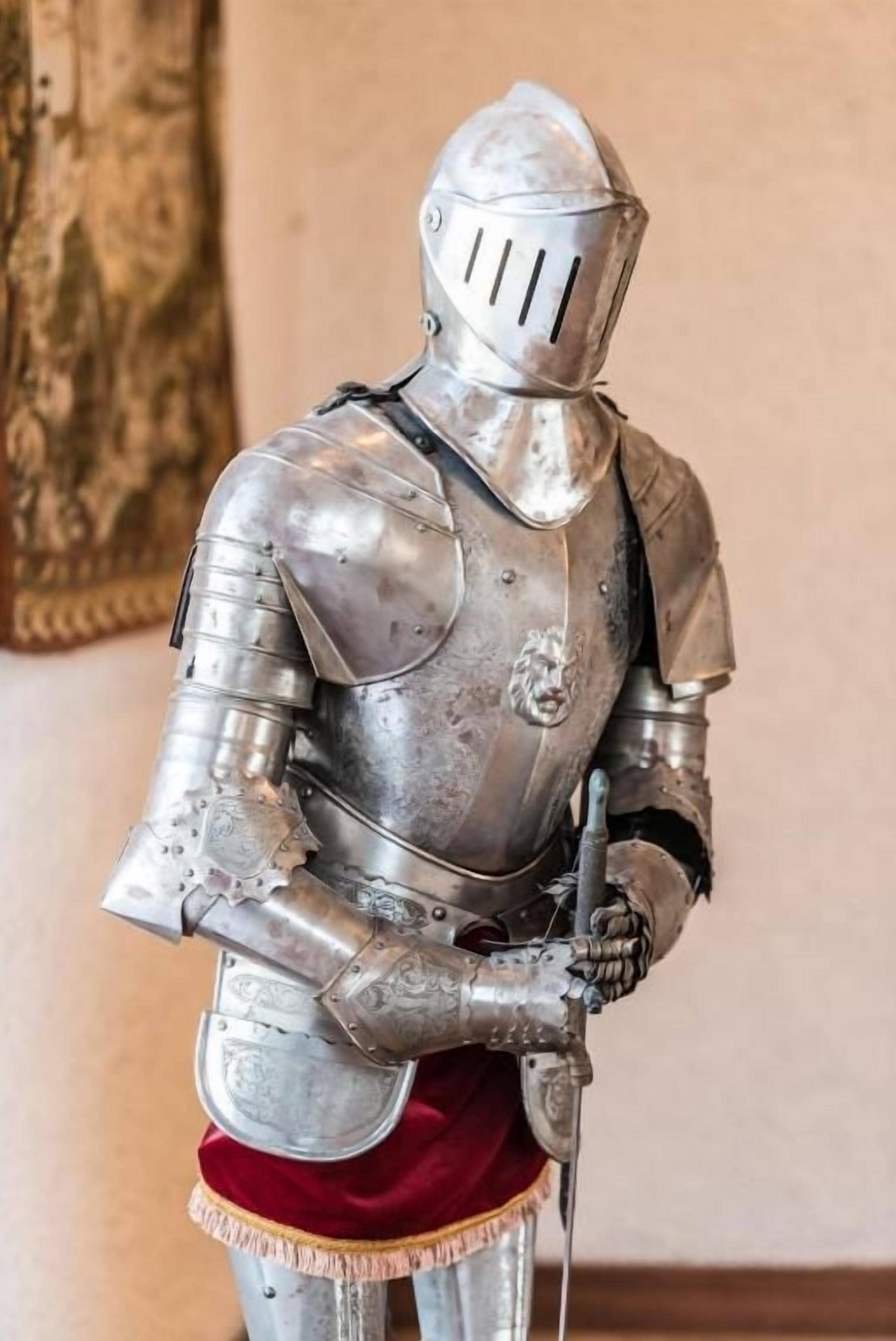 A medieval knight's armor with a sword, standing against a plain wall.
