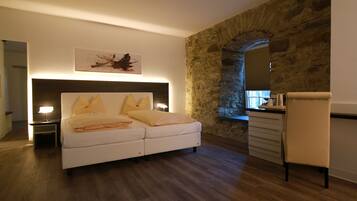 Un dormitorio moderno con pared de piedra, una cama con ropa de cama blanca, un escritorio con silla y un cuadro en la pared.