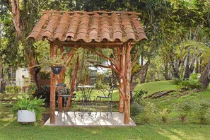 A gazebo with a tiled roof, surrounded by lush greenery and a small patio area with a table and chairs. - Hotel Yalconia (San Agustin)
