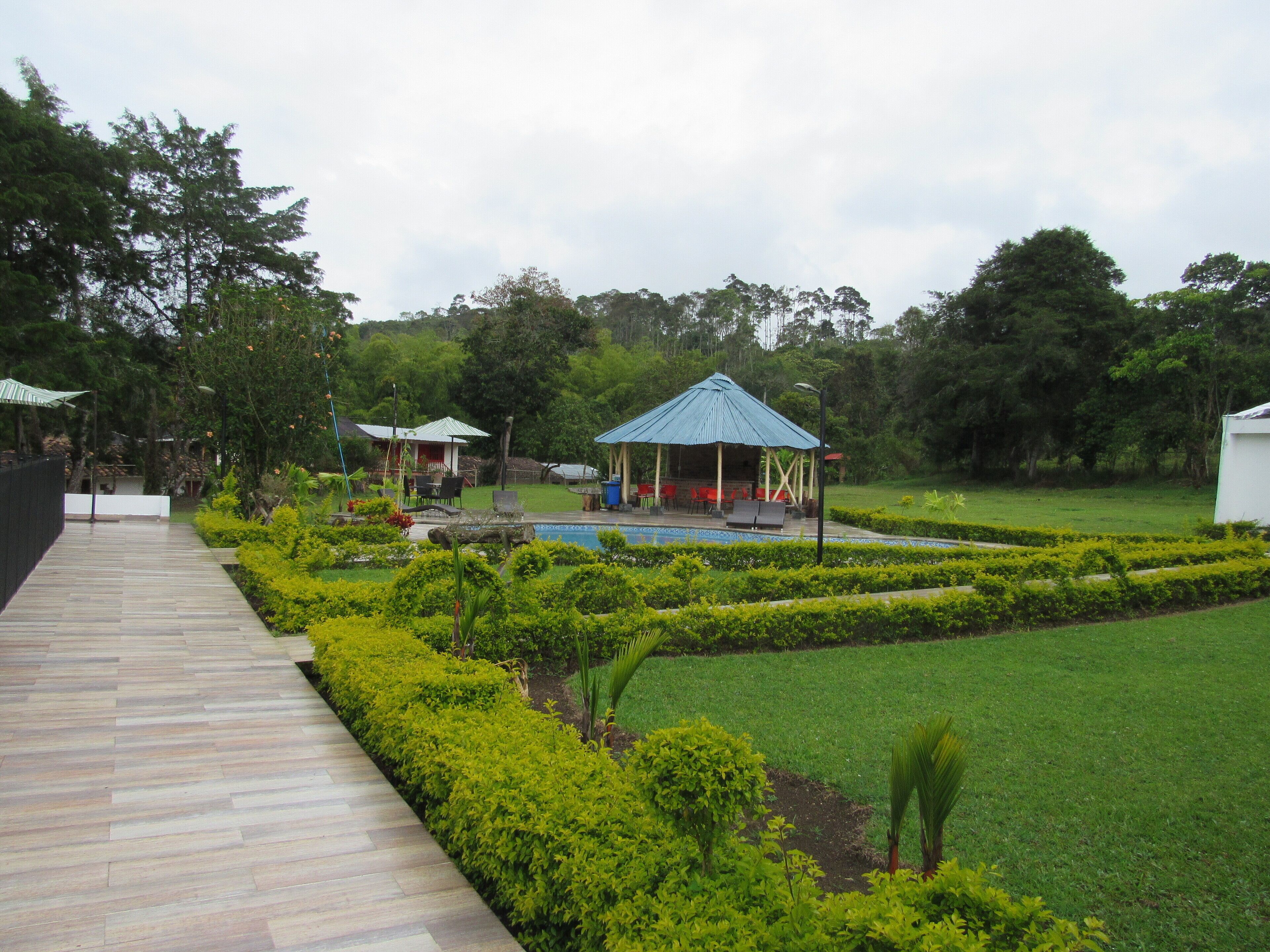 Un jardín ajardinado con piscina, un pabellón y un camino pavimentado.
