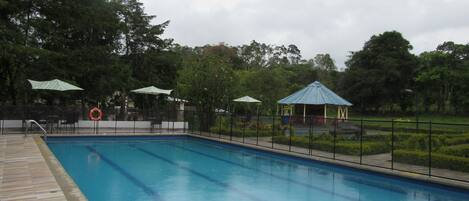 Una piscina con muelle de madera, rodeada por una valla y protegida por sombrillas.