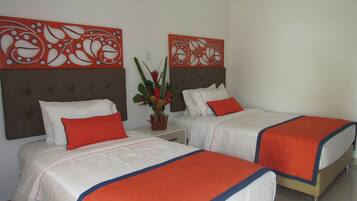A hotel room with two beds, each with white bedding and orange accents, a decorative wall panel, and a small plant on the nightstand.