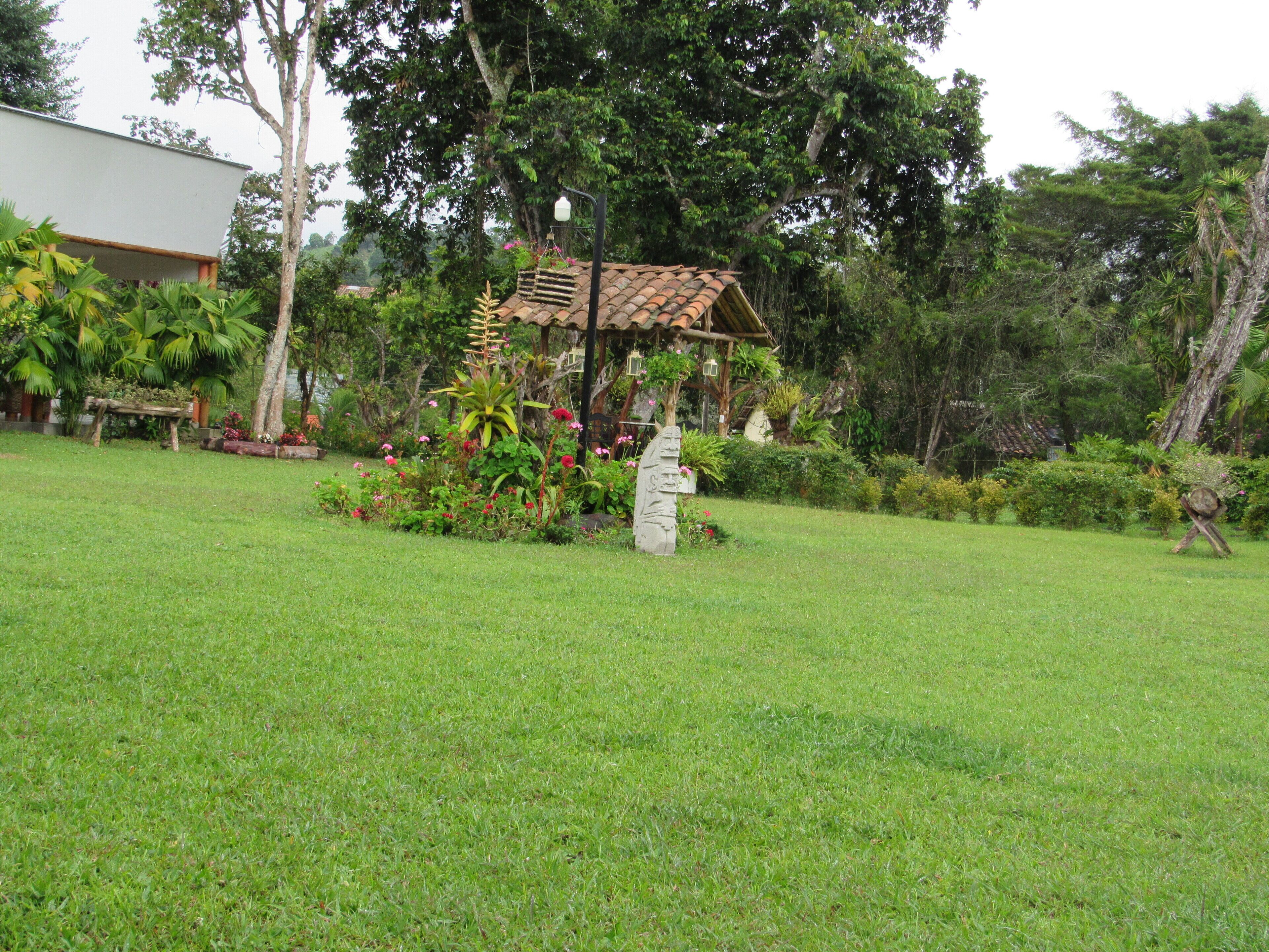 A garden with a gazebo, a stone sculpture, and a variety of plants and flowers.