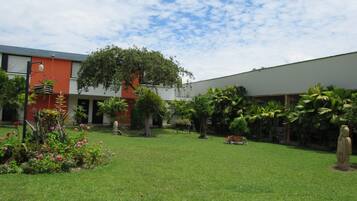 A courtyard with a lawn, a large tree, and a building with a red facade.