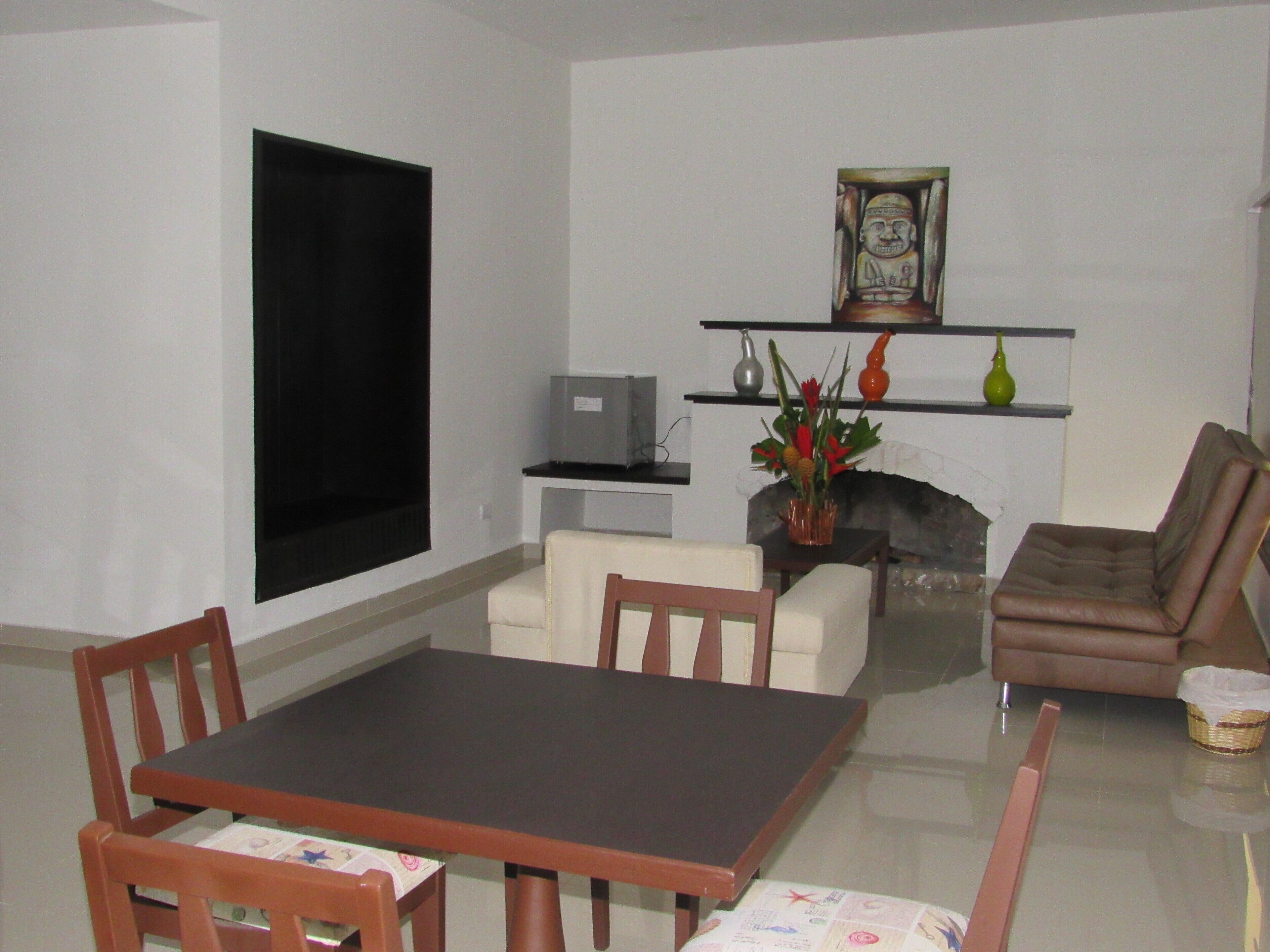 Una sala de estar con una mesa de comedor, sillas, un sofá, una chimenea y objetos decorativos en estantes.