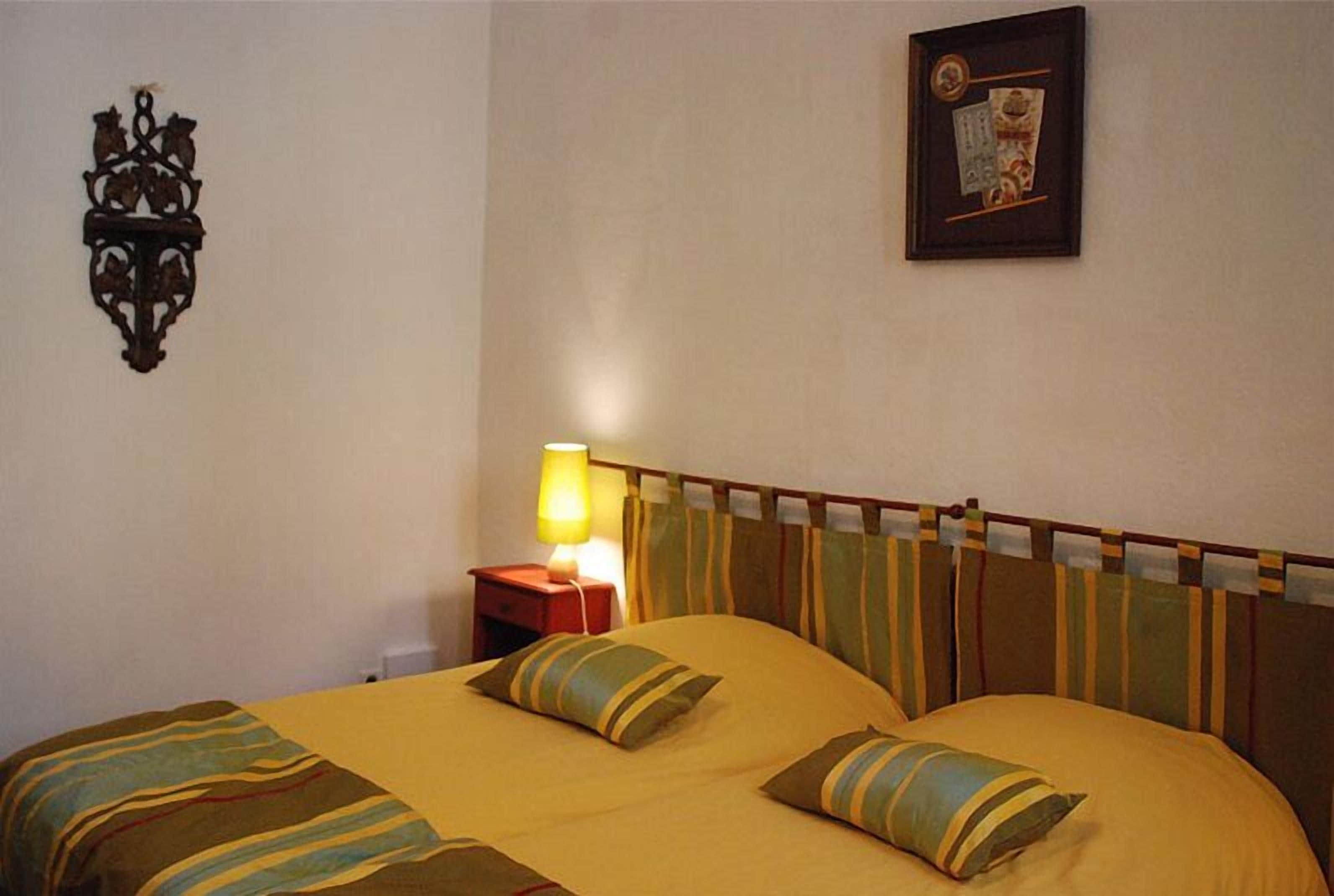 Una cama con ropa de cama y almohadas a rayas, una lámpara de noche, un certificado en un marco en la pared y un adorno decorativo en la pared.