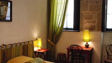 Una stanza con un letto, due comodini con lampade, uno sgabello e una finestra con tende.