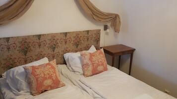 A double bed with floral headboard, two pillows, a nightstand, and a chandelier.