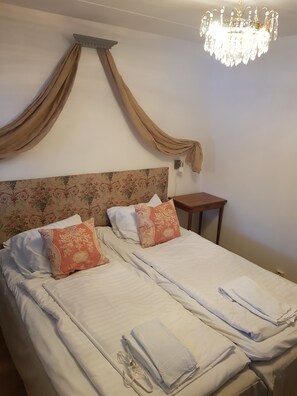 A double bed with floral headboard, two pillows, a nightstand, and a chandelier. - Big Moose Hotel (Asarna)