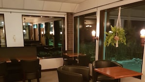 Een modern restaurant met een combinatie van zitplaatsen in cabines en aan tafels, grote ramen en een hangplant.
