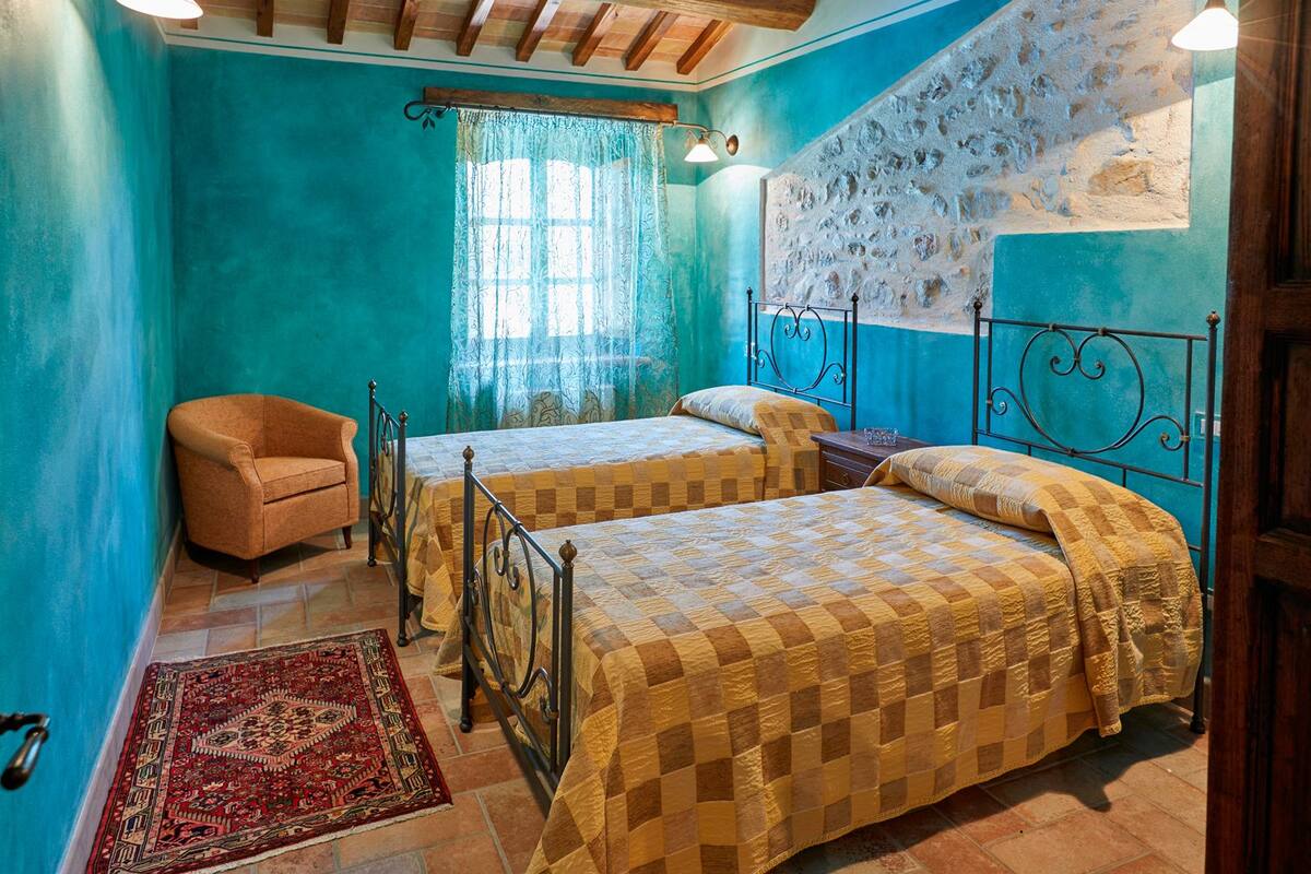 A bedroom with two beds, a chair, and a decorative wall.