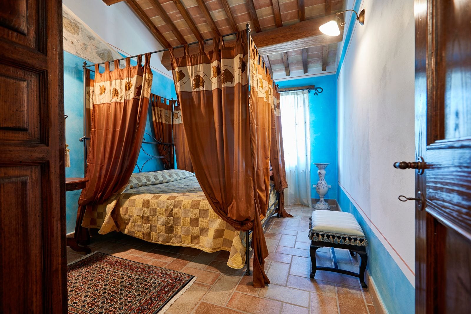 Een slaapkamer met een hemelbed, een klein bankje, een decoratieve vaas en een betegelde vloer.