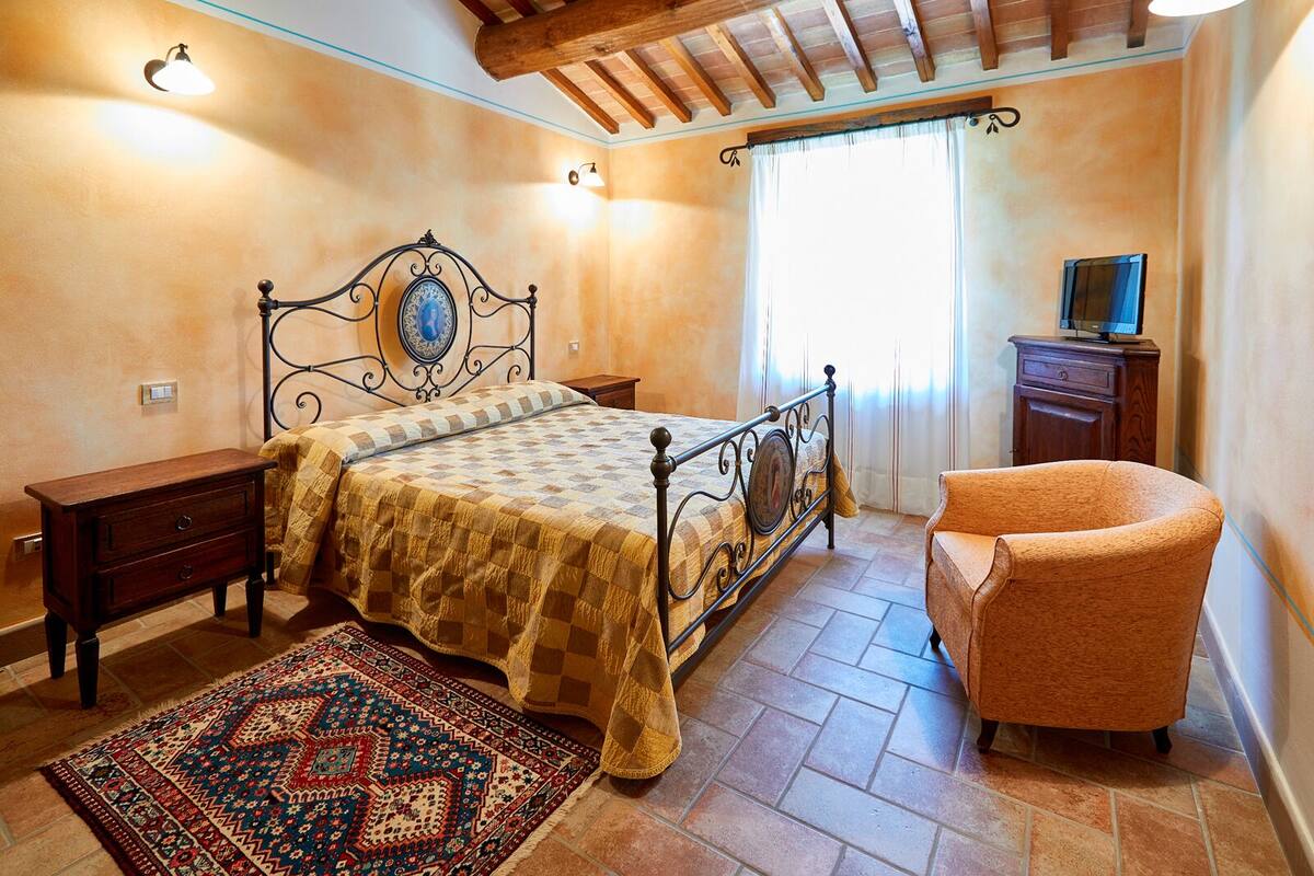 A bedroom with a bed, a chair, a nightstand, a dresser, and a window with curtains.