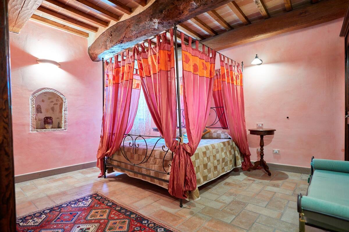 A bedroom with a four-poster bed, a small table, a chair, and a decorative rug.