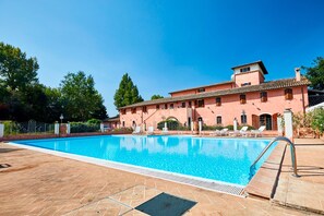 A swimming pool with a tiled deck, a building with a pink facade, and a clear blue sky. - Agriturismo Il Molino Antico (Spoleto)