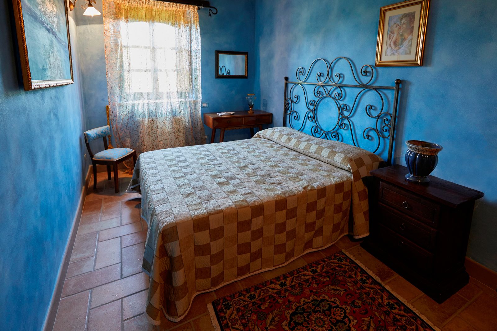 A bedroom with a checkered bedspread, a wooden nightstand, a chair, a dresser, and a patterned rug.
