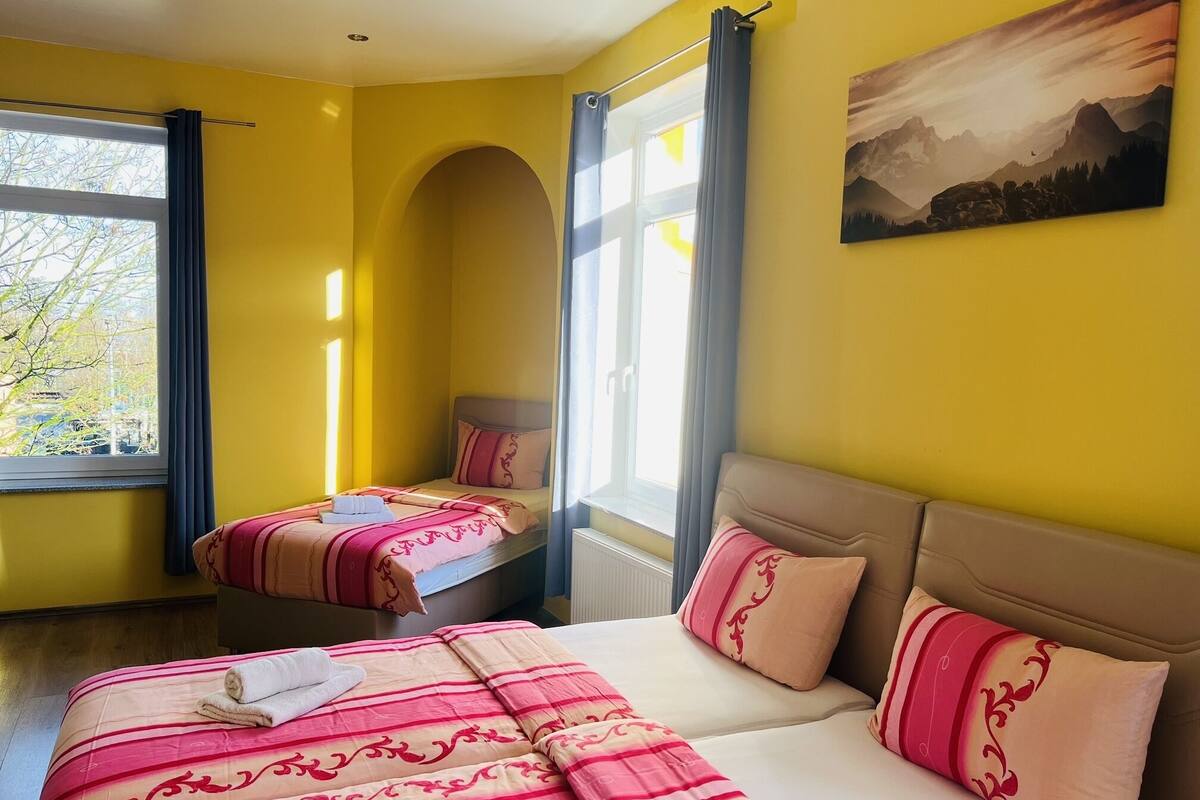 A hotel room with two beds, a large window, and a painting on the wall.