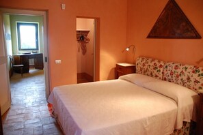 A bedroom with a bed, a desk, and a chair. There is a window and a door leading to another room. - Verdidea - Bagnoletto (Orte)