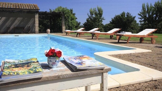 Ein Poolbereich mit Liegestühlen, einem Tisch mit Zeitschriften und Blumen, und ein Gebäude im Hintergrund.