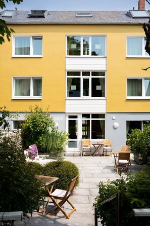 A yellow two-story building with a central entrance, large windows, and a small patio area with outdoor furniture. - Haus Miramar (Helgoland)