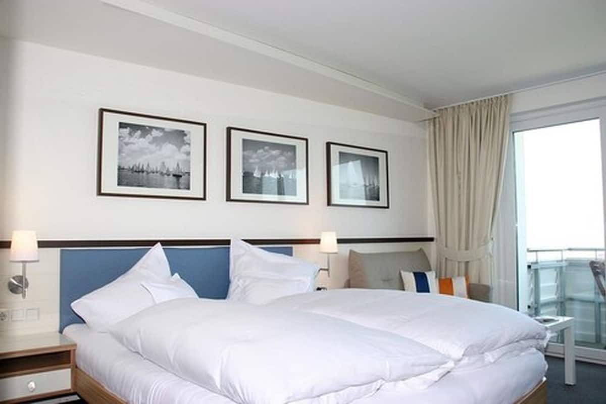 Quarto de hotel com uma cama grande, duas mesas de cabeceira, uma janela com cortinas e três quadros na parede.