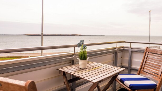 Una mesa de madera con una planta en maceta, una silla acolchada y vistas al mar.