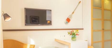 Habitación de hotel con cama, una mesita, una silla, televisor, guitarra, jarrón con flores y un armario.