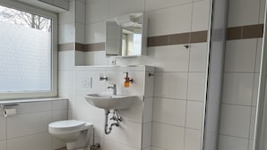 A modern bathroom with a toilet, sink, and shower. - M&M Hotel - Neu Wulmstorf (Neu Wulmstorf)