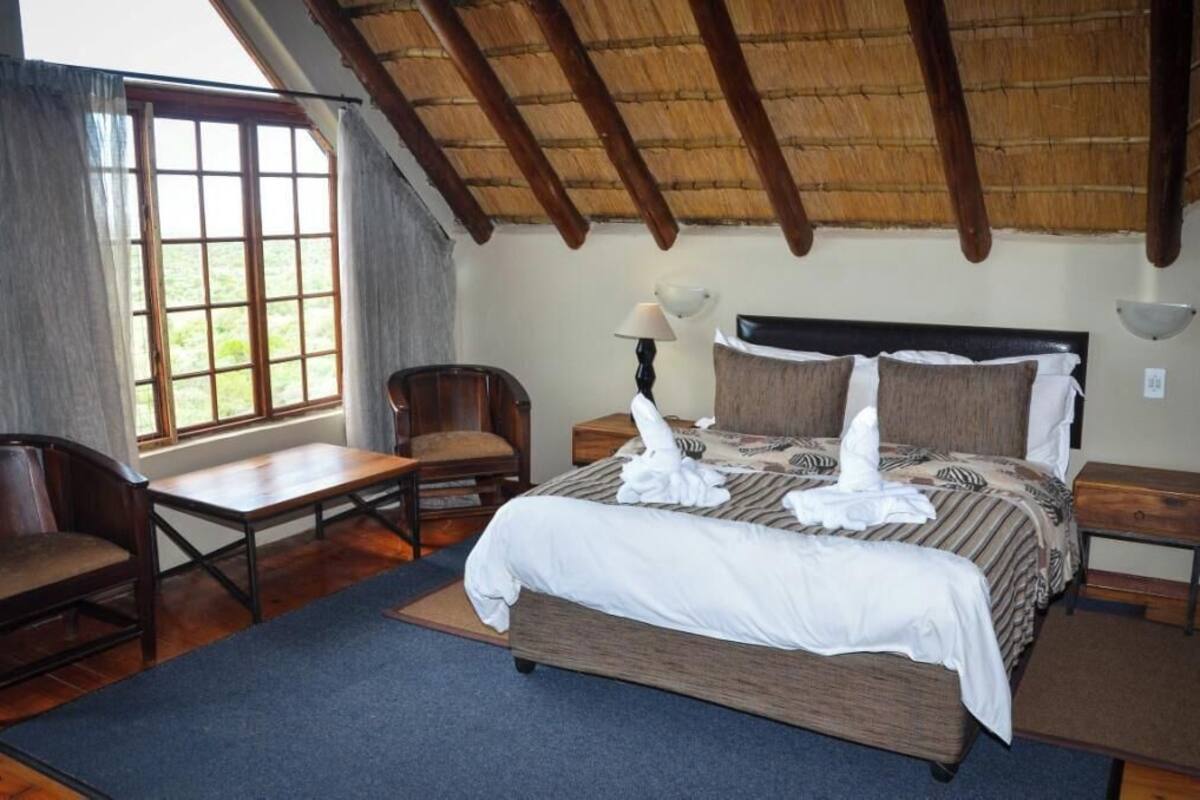 A hotel room with a bed, a chair, a table, and a window with curtains.