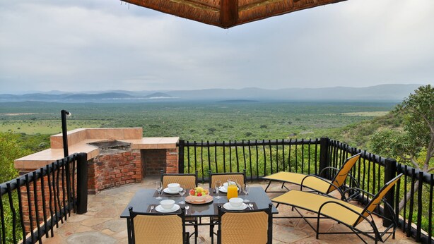 Un espacio exterior para comer con una mesa dispuesta para dos, un horno de ladrillo y vistas al paisaje.