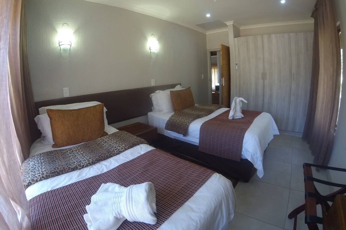 A hotel room with two beds, each with a headboard, a flat-screen TV, and a ceiling fan.