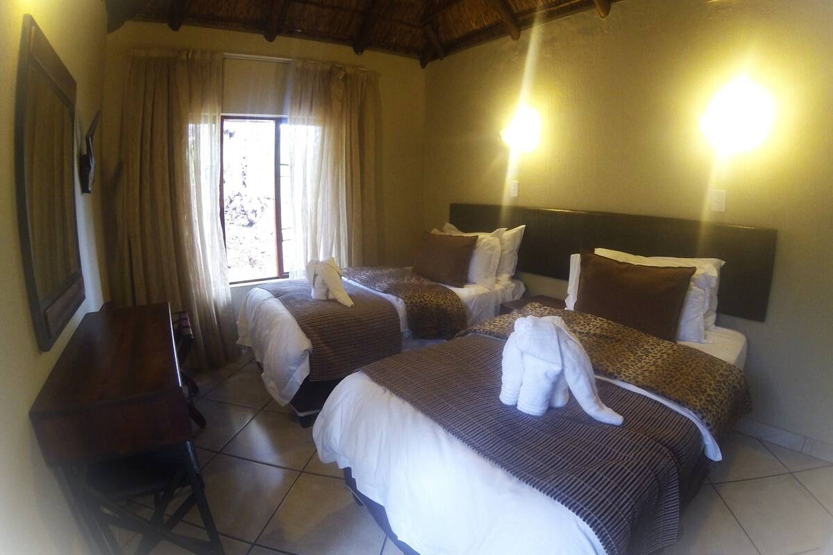 A hotel room with two beds, a desk, and a window with curtains.