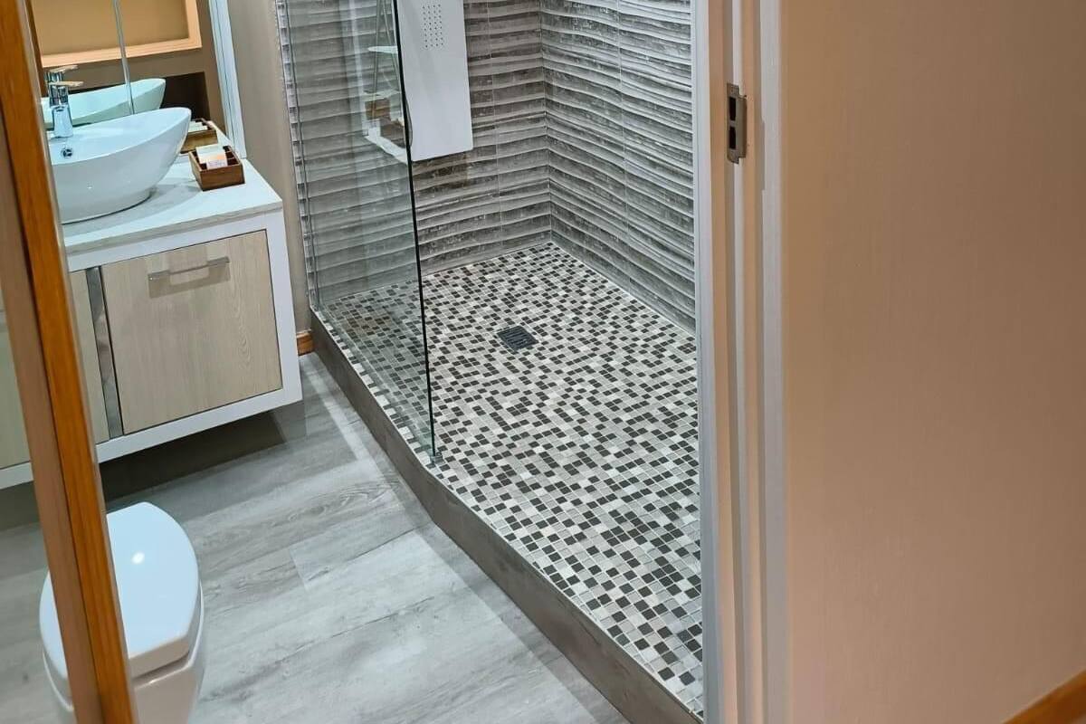 A modern bathroom with a glass-enclosed shower, a white sink, and a tiled floor.