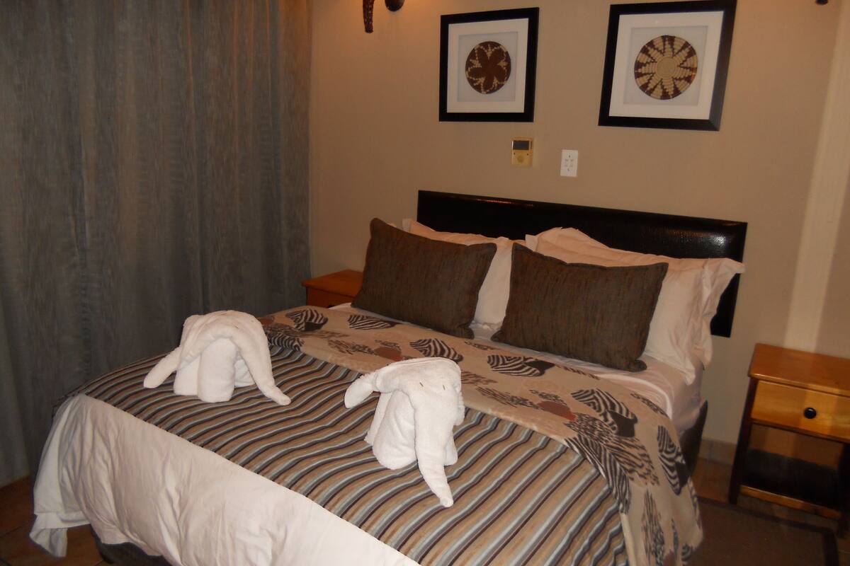 A hotel room with a bed, pillows, and two framed pictures on the wall.