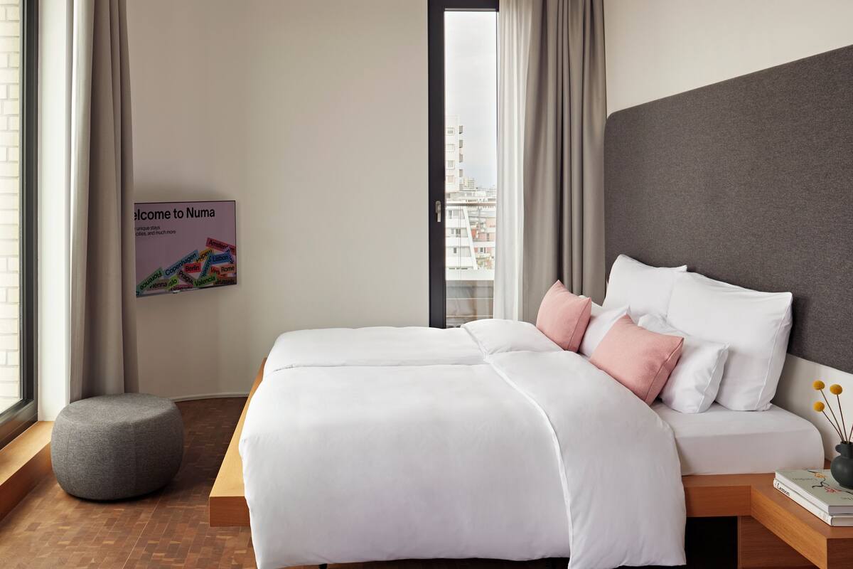 Una habitación de hotel moderna con una cama grande, un banco de madera y vistas a la ciudad.