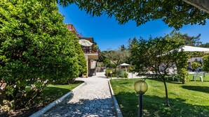 A stone pathway leading to a building with a balcony and outdoor seating area. - Da Milena (Orbetello)
