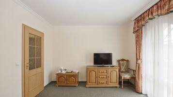 A room with a wooden cabinet, a television, a chair, and a window with curtains.