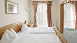 Habitación de hotel con cama doble, mesita de noche, lámpara, un cuadro en la pared y vistas al exterior a través de amplias ventanas con cortinas.