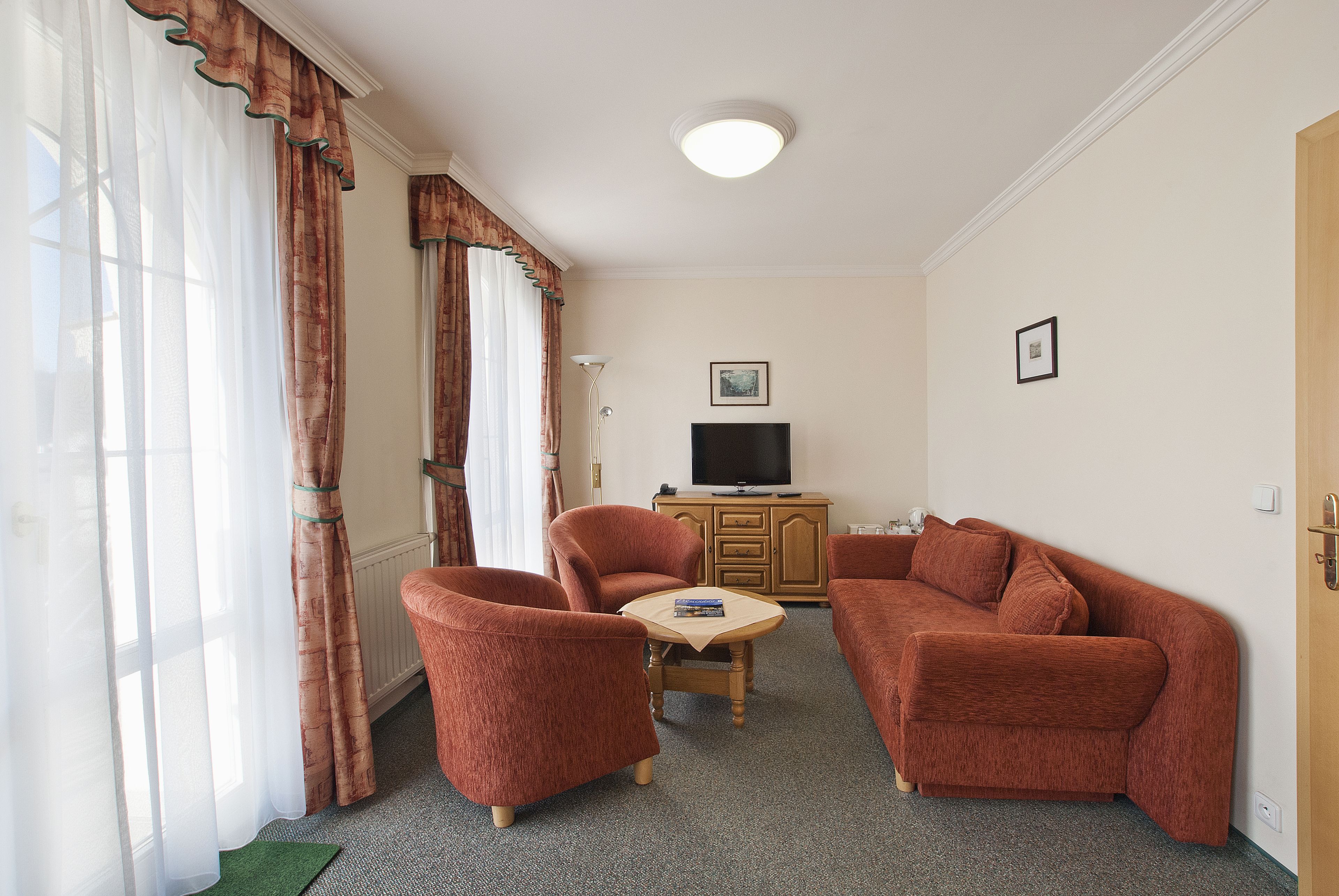 A living room with a sofa, two armchairs, a small table, a television, and a cabinet.