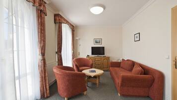 A living room with a sofa, two armchairs, a small table, a television, and a cabinet.